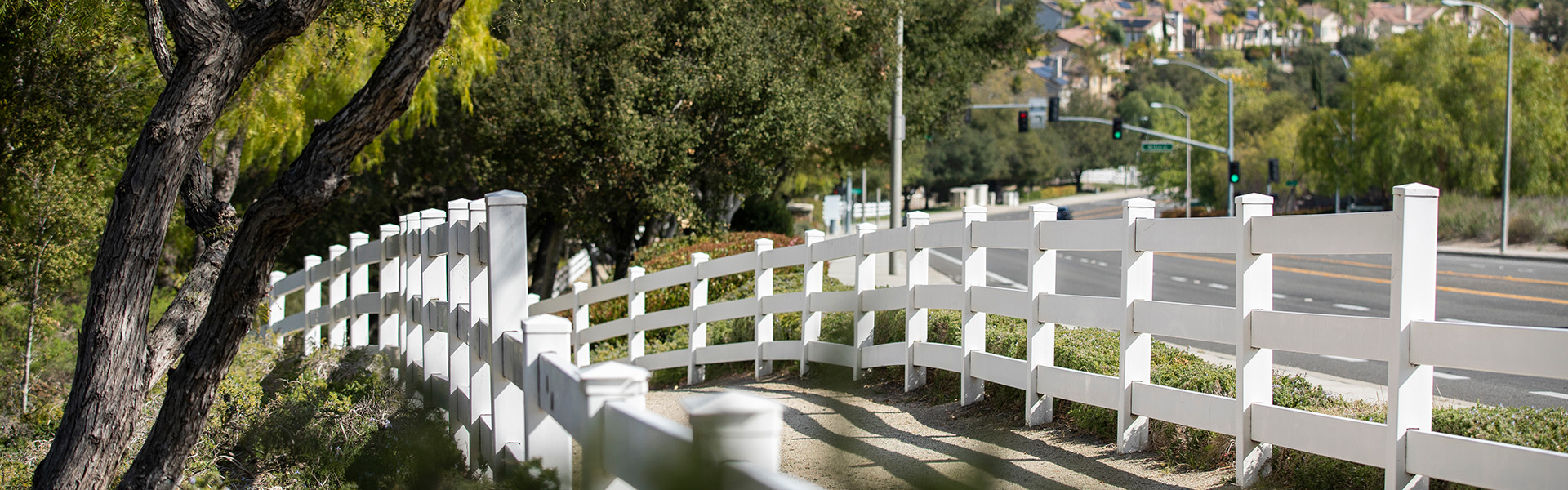 Pepper trees and a white fence frame a public sidewalk in Coto de Caza, California, USA.